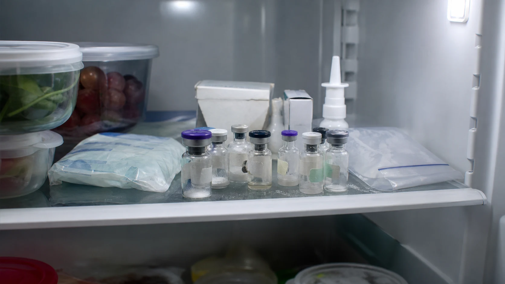 A normal home refrigerator shelf crowded with several peptide vials, small boxes, an ice pack and loose packaging